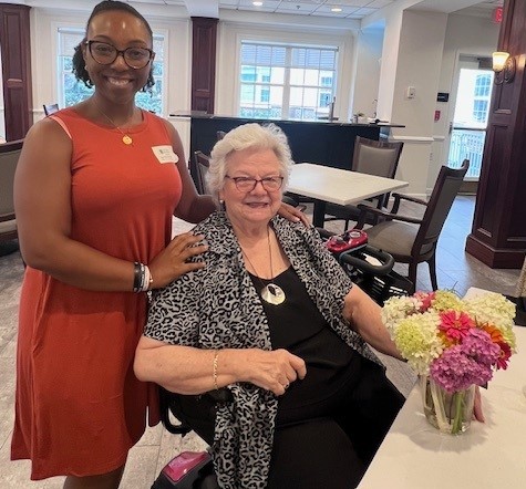 African American woman standing next to seated older white woman