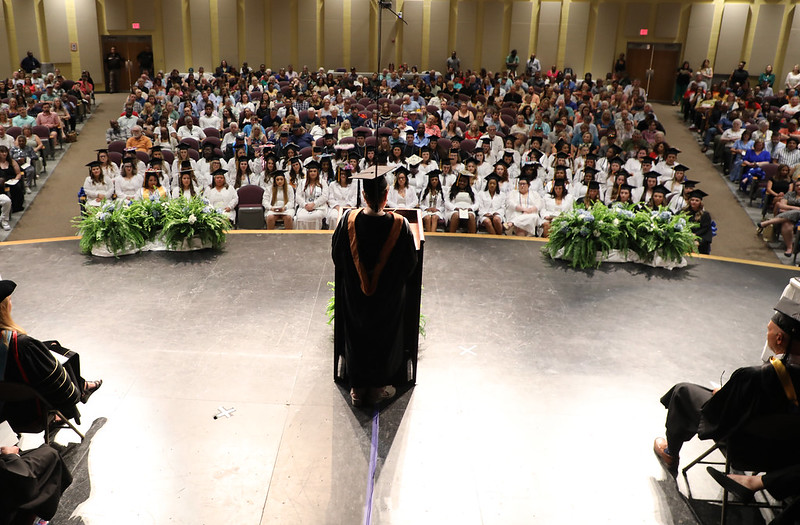 graduates wearing white coats facing stage